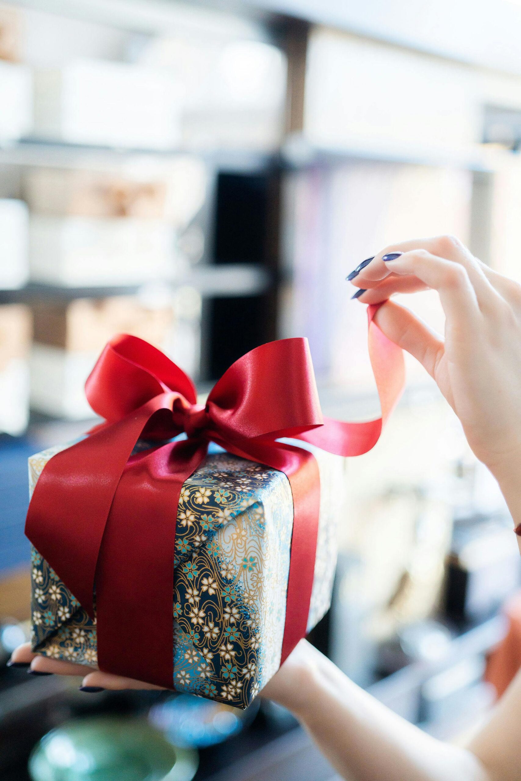 Close-up of a woman unwrapping a beautifully decorated gift box with a red ribbon indoors.