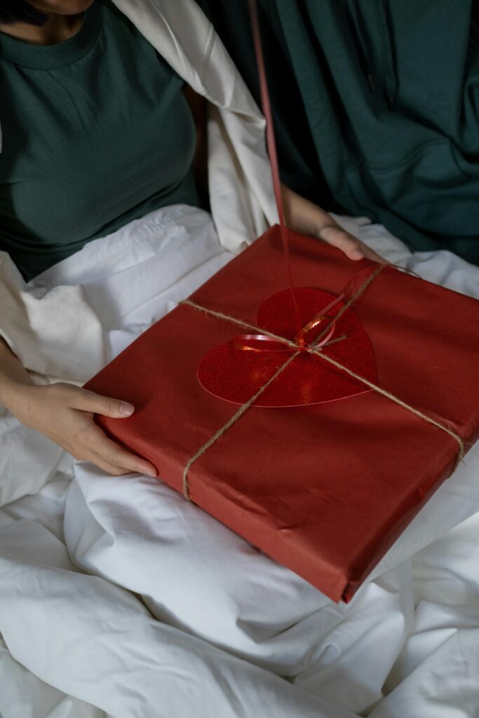 A person holding a wrapped present with a red heart in a cozy setting.